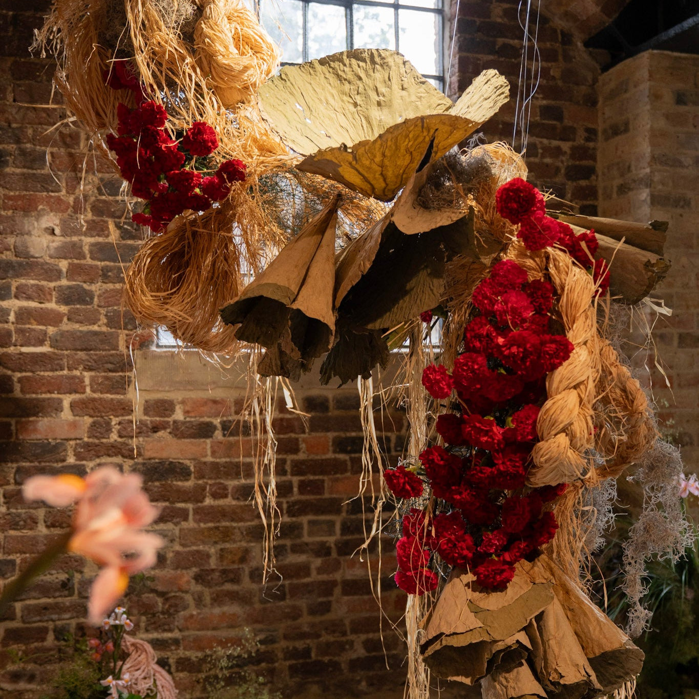 Decorative hanging with red flowers and gold leaves against a brick wall.